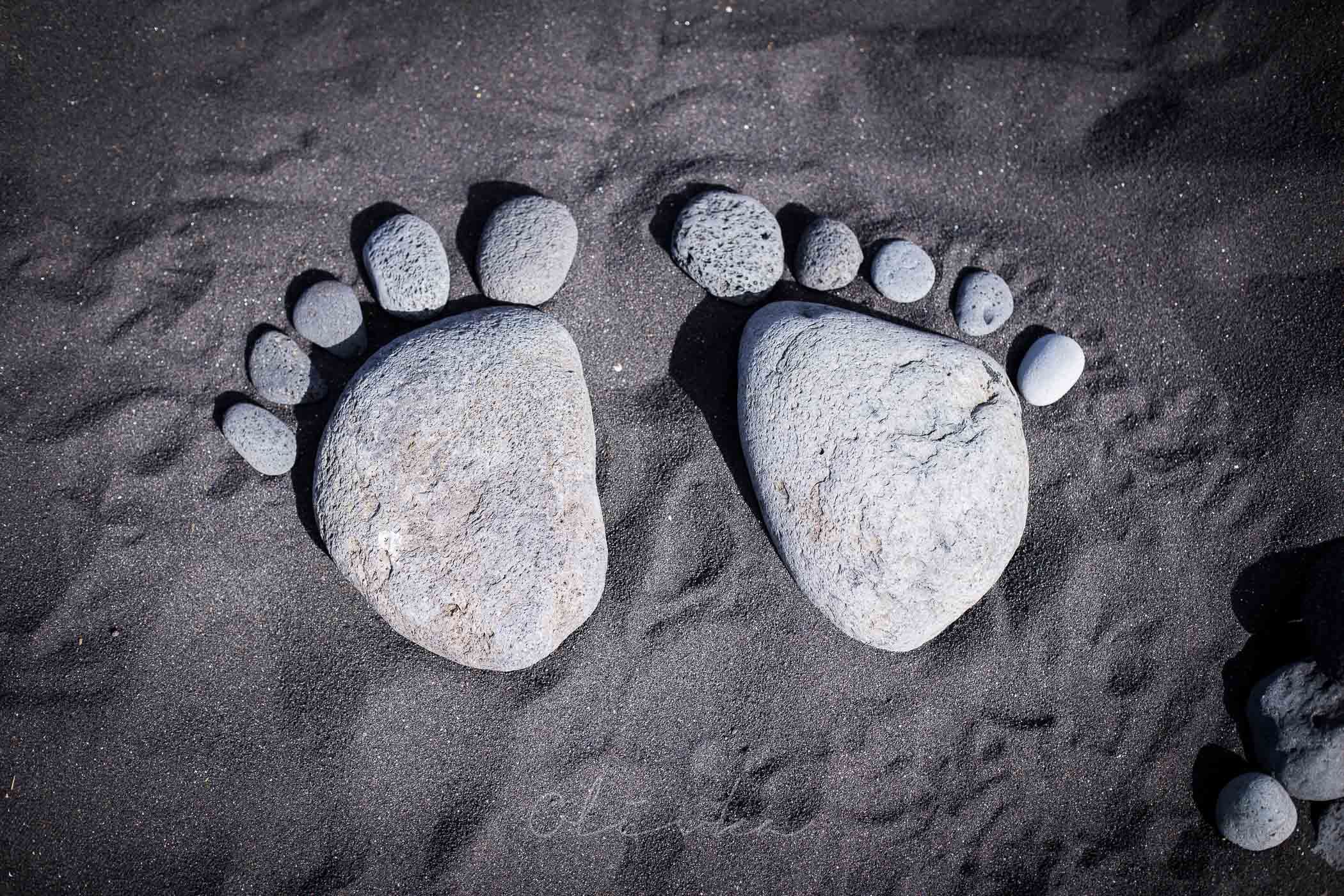 Ślady stóp ułożone z kamieni ma czarnym piasku